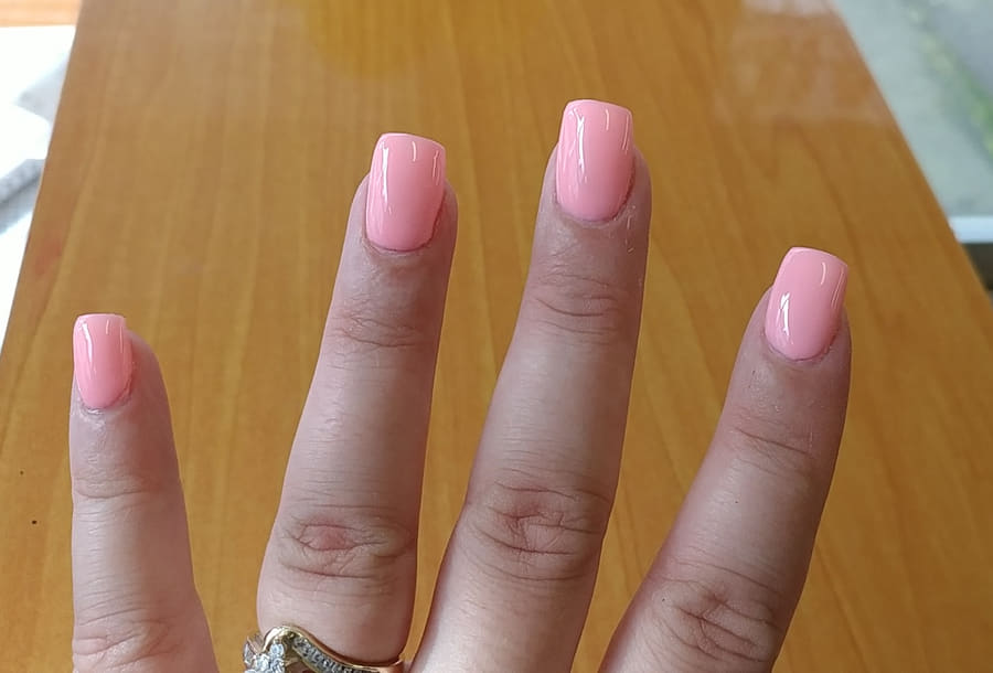 Squared coral gel nails on the wooden manicure table by the window