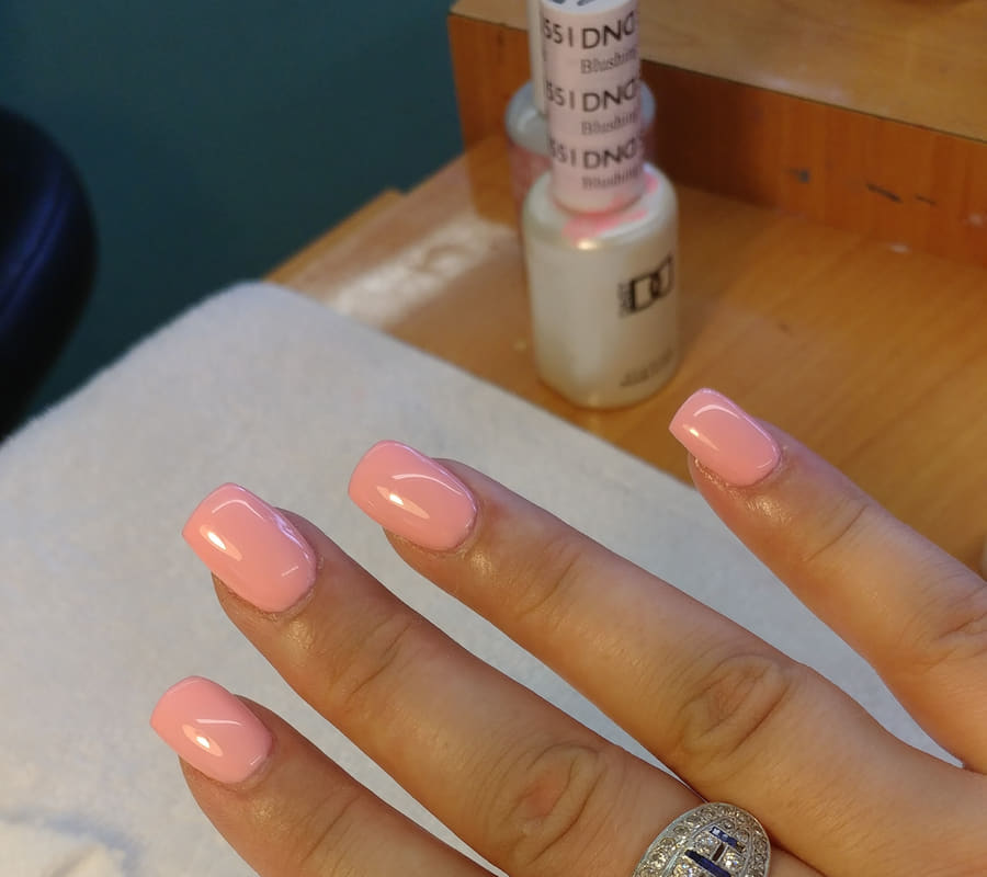 Peach gel nails on the manicure table beside the polish bottle they were painted from
