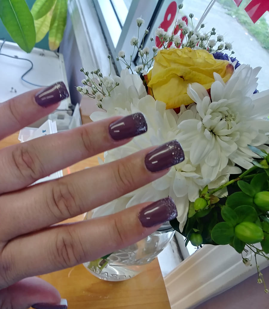 Deep plum gel nails photographed beside white chrysanthemums on the salon windowsill